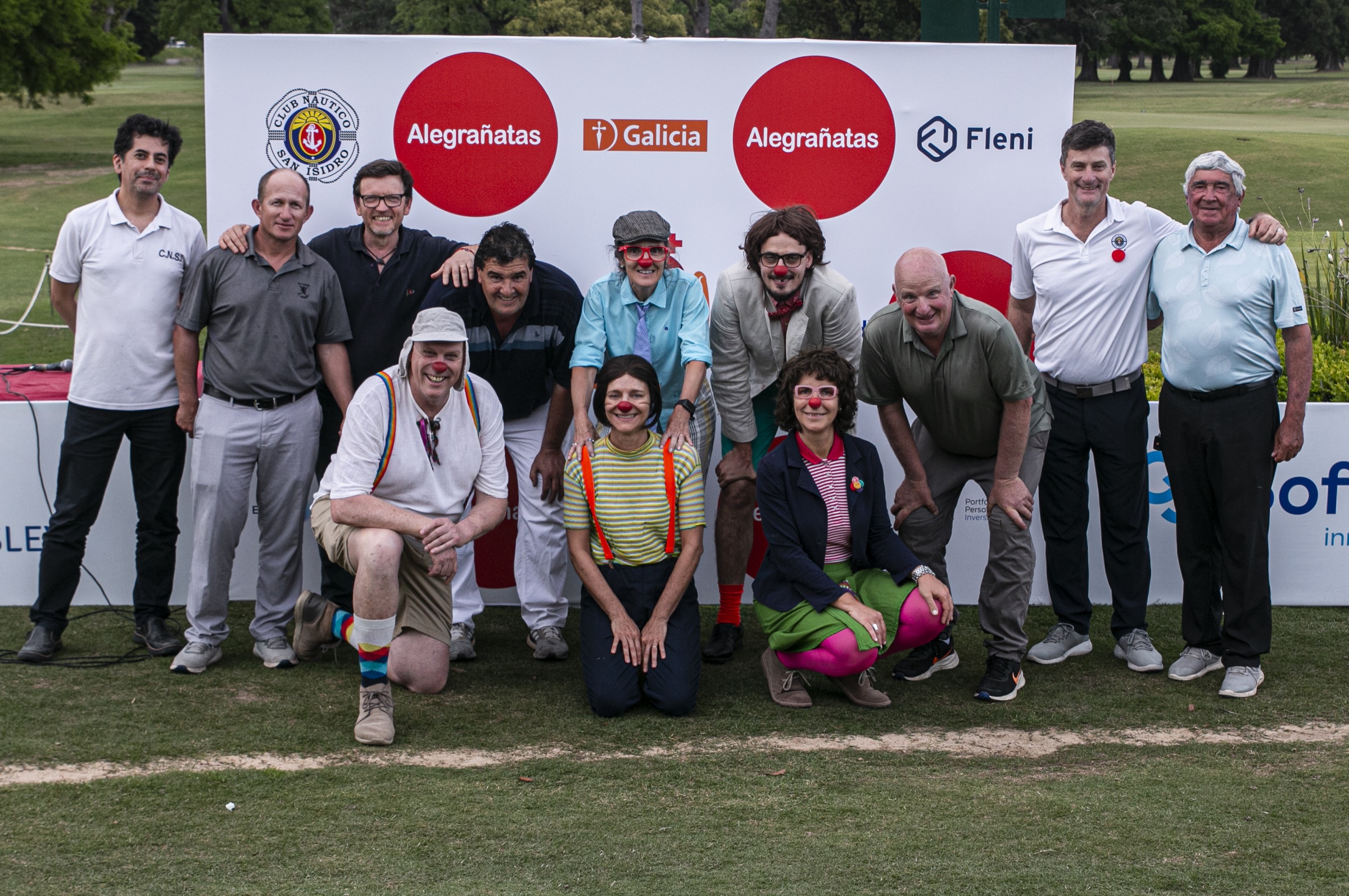 Golfistas y payasos de Alegrañatas junto al backdrop de sponsors de la Copa